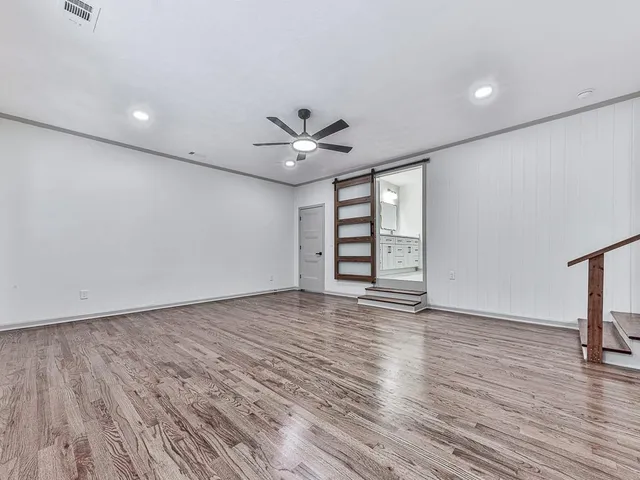 an empty room with wooden floor chandelier fan and windows