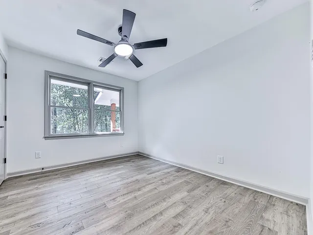 an empty room with wooden floor ceiling fan and windows