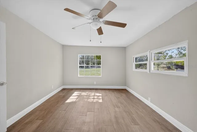 an empty room with wooden floor ceiling fan and windows