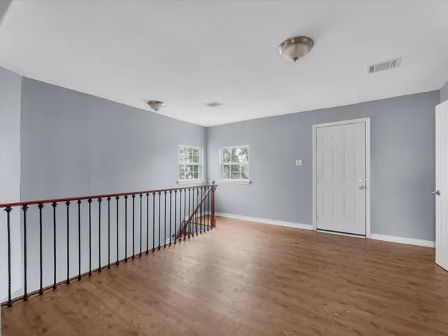 an empty room with wooden floor chandelier fan and windows