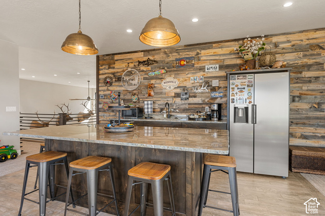 1192 East Ashdown Road Cedar City, UT 84721 - Photo 74 of 96 Expansive kitchen island with a stone-finish countertop, custom wood-paneled wall, stainless steel side-by-side refrigerator, recessed lighting, and industrial-style pendant lighting