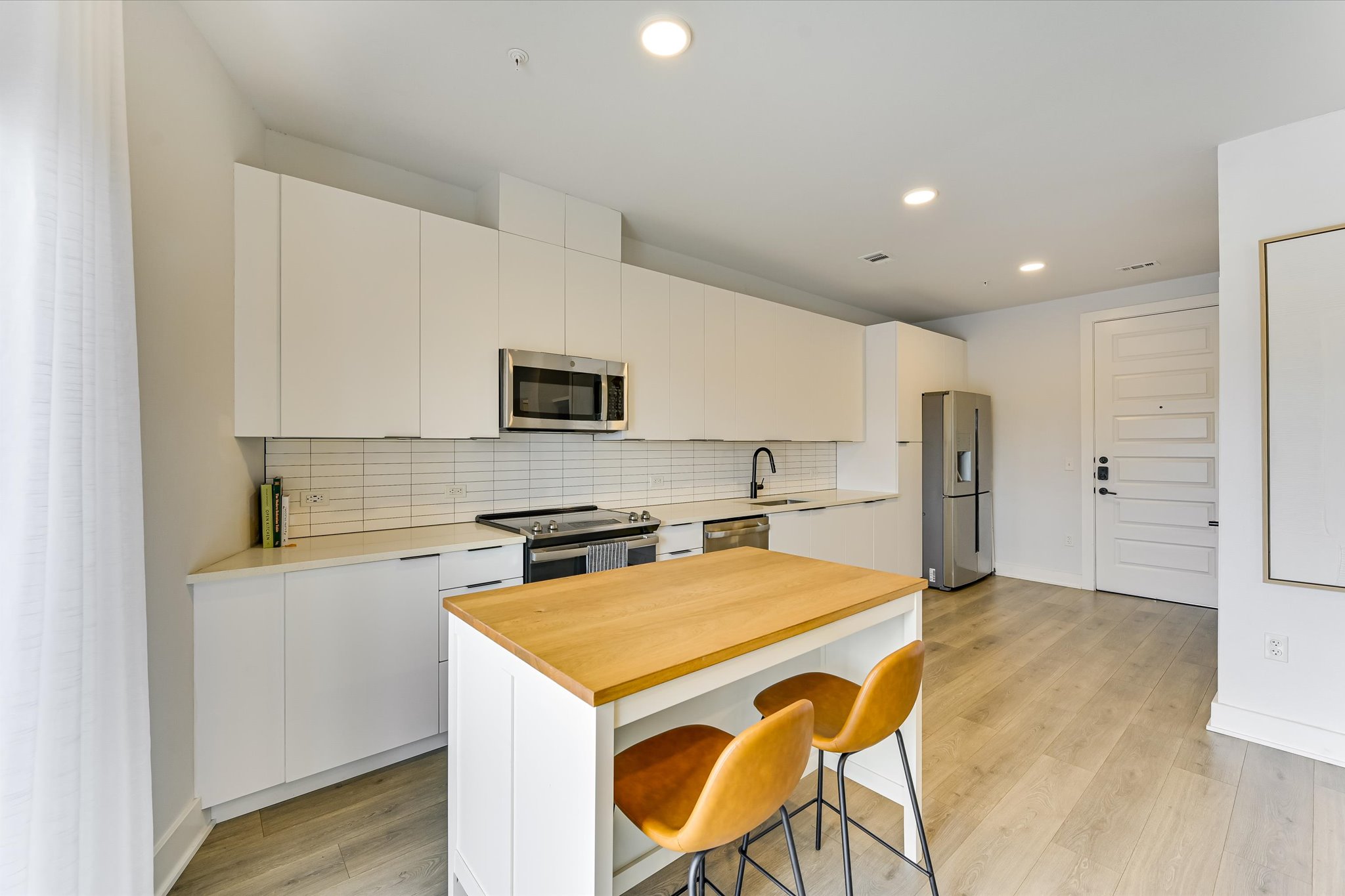 2220 Webberville Road, Unit 308 Austin, TX 78702 - Photo 5 of 21 Modern kitchen featuring white flat-panel cabinetry, a wood-finish island with seating, stainless steel appliances, a subway tile backsplash, and light wood-finish flooring