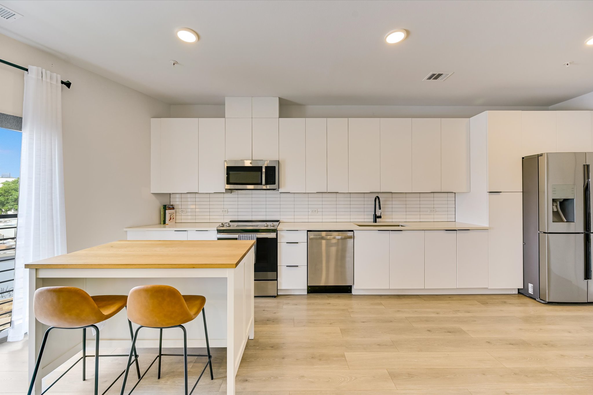2220 Webberville Road, Unit 308 Austin, TX 78702 - Photo 6 of 21 Modern kitchen featuring light wood-finish flooring, white flat-panel cabinetry, stainless steel appliances, a subway tile backsplash, and a kitchen island with a light wood countertop