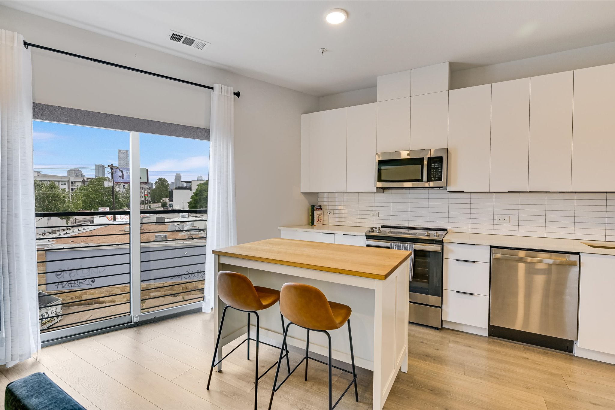 2220 Webberville Road, Unit 308 Austin, TX 78702 - Photo 7 of 21 Modern kitchen featuring wood-finish flooring, white cabinetry, a wood-top island, stainless steel appliances, and a tiled backsplash