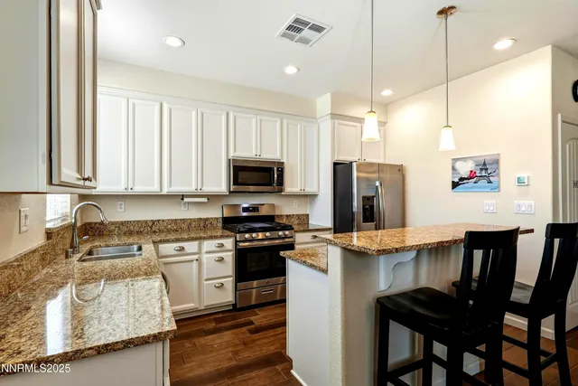 a kitchen with stainless steel appliances granite countertop a stove top oven a sink refrigerator and white cabinets with wooden floor