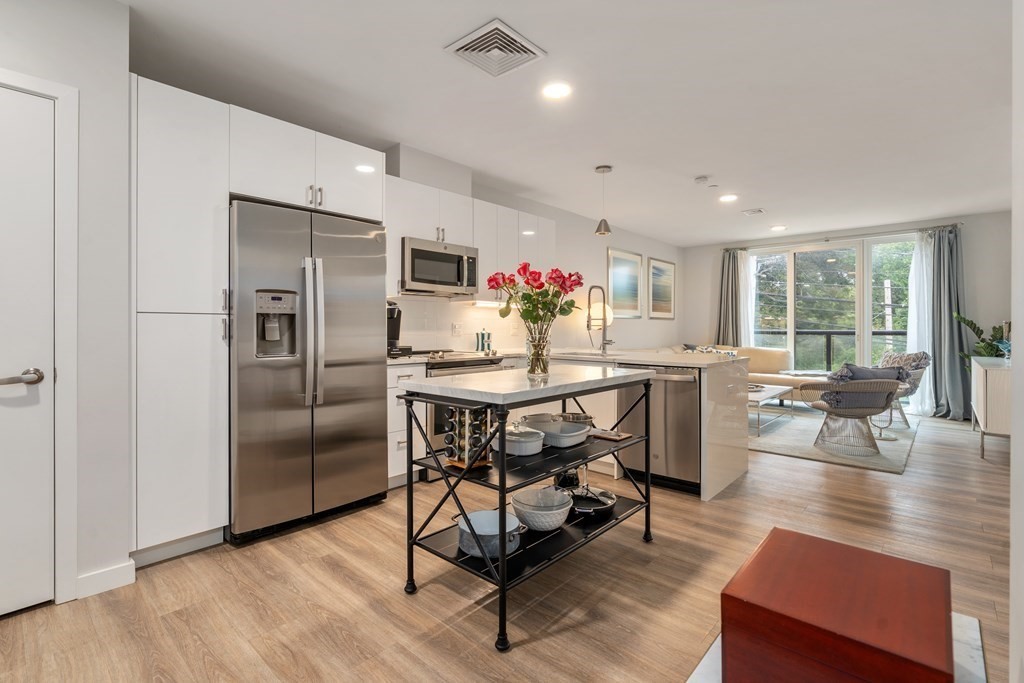 a kitchen with stainless steel appliances kitchen island granite countertop a refrigerator a stove a dining table and chairs with wooden floor