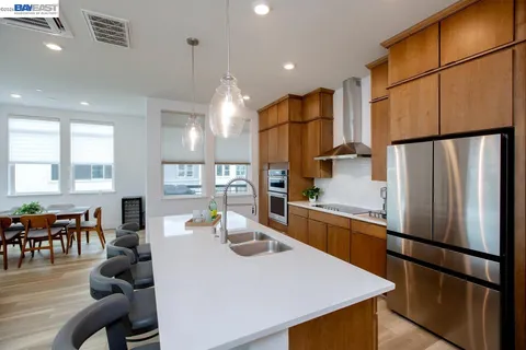 a kitchen with stainless steel appliances a refrigerator a stove a dining table and chairs with wooden floor