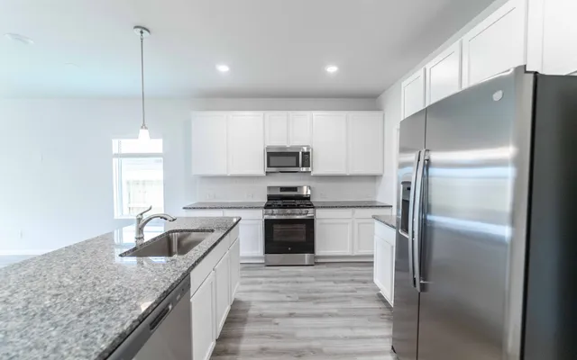 a kitchen with stainless steel appliances granite countertop a refrigerator a sink a stove and oven