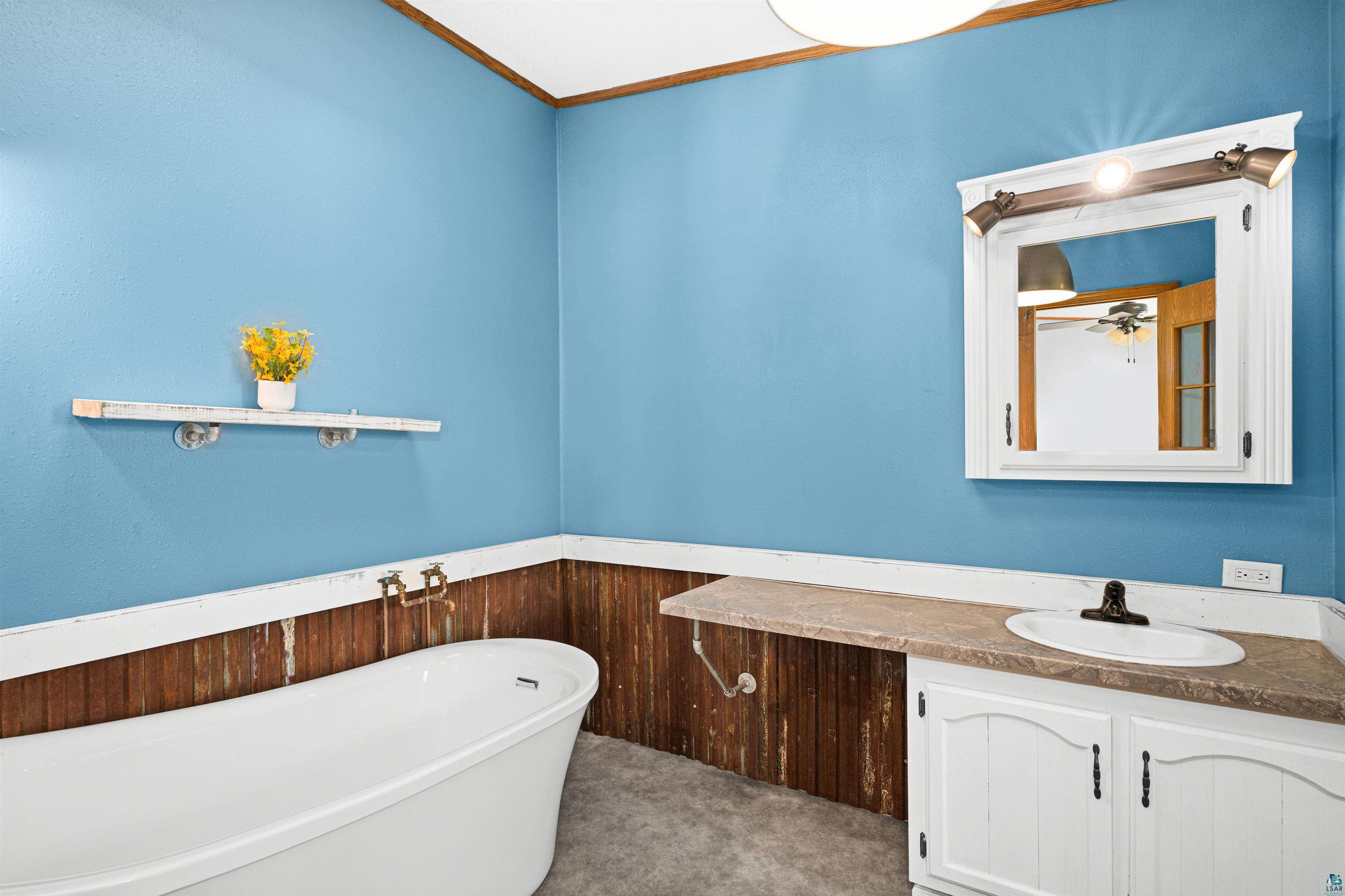 3126 Beyer Road Duluth, MN 55804 - Photo 18 of 23 Walk-in bathroom featuring a freestanding soaking tub, single vanity with countertop, framed mirror with integrated lighting, and a wall-mounted shelf