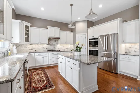 a kitchen with granite countertop a refrigerator oven a sink dishwasher and white cabinets with wooden floor