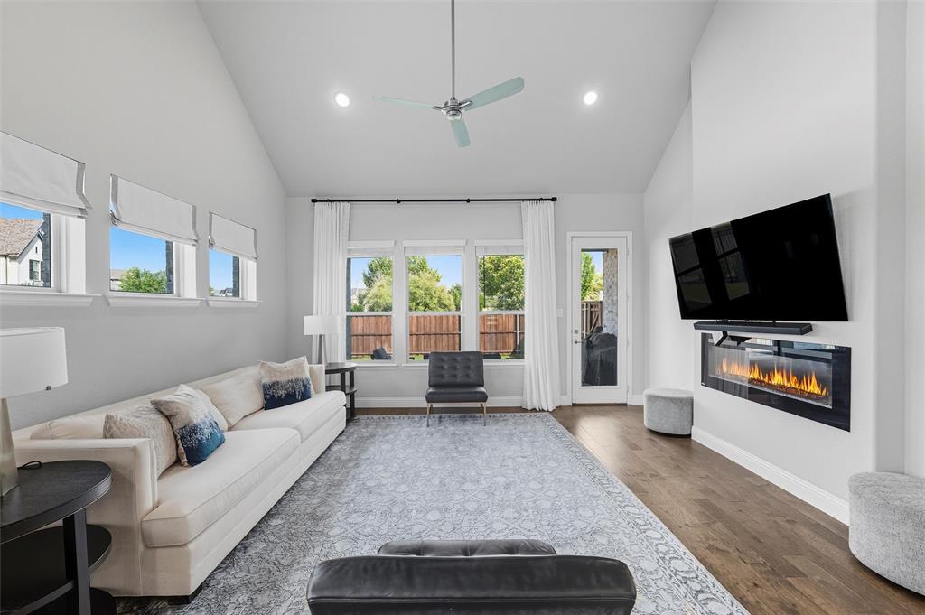 8492 Chapote Road Frisco, TX 75035 - Photo 14 of 40 Living Area features vaulted ceiling with exposed beam and ceiling fan. Decorative fireplace as the focal point. Open layout providing ample space for seating arrangements. Wide-plank hardwood flooring extending through the space.