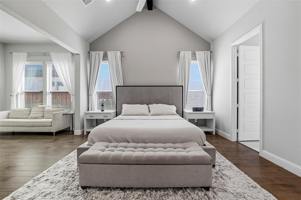 8492 Chapote Road Frisco, TX 75035 - Photo 15 of 40 Primary Bedroom features vaulted ceiling with exposed beam and ceiling fan. Spacious layout with open entry to a sitting area. Wide-plank hardwood flooring extending through the space.
