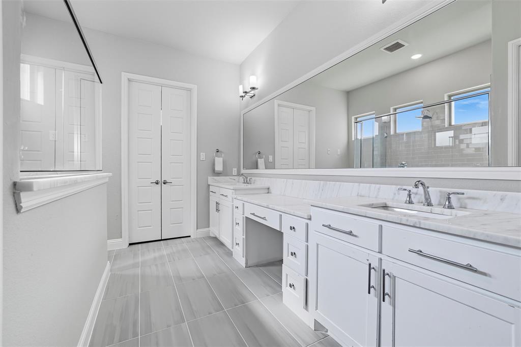 8492 Chapote Road Frisco, TX 75035 - Photo 18 of 40 Primary Bathroom features modern light fixtures above expansive mirrors. Dual sinks with quartz countertops and built-in vanity. Frameless glass shower enclosure with tile surround and separate soaking tub. Large-format tile flooring extending through the space.