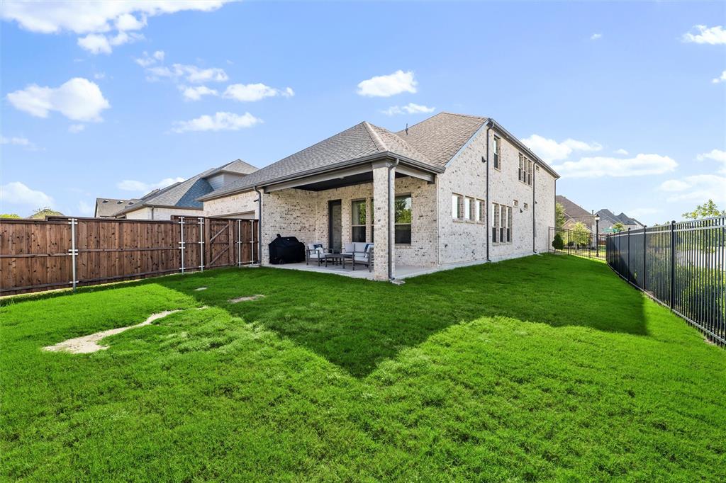 8492 Chapote Road Frisco, TX 75035 - Photo 28 of 40 Backyard features covered patio with concrete flooring and open space for seating. Fully fenced yard with wood privacy fence on one side and metal fence on the other. Expansive green lawn extending across the area.