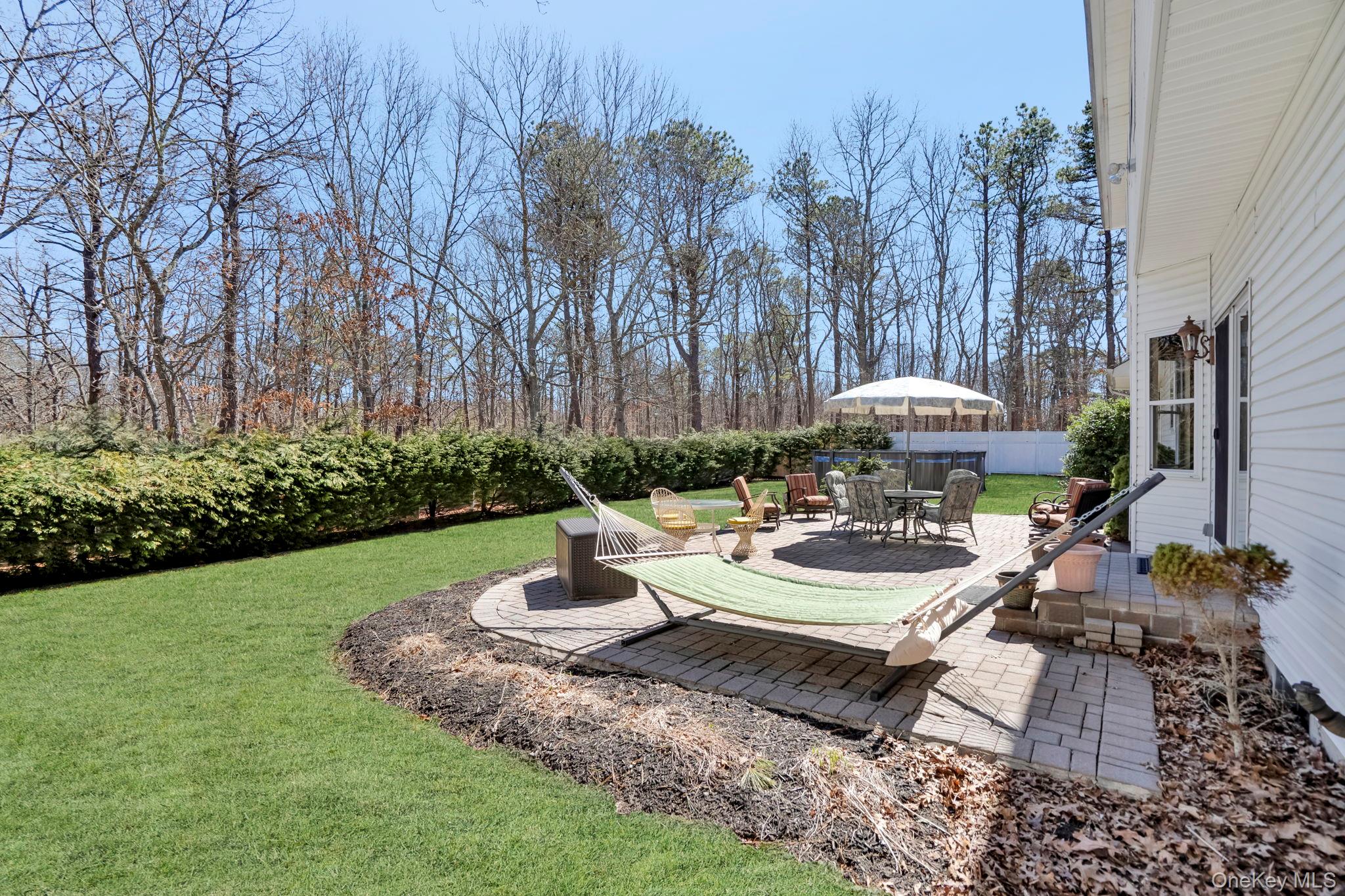 20 Ricky Road Manorville, NY 11949 - Photo 27 of 27 a view of a patio with couches table and chairs under an umbrella with large trees