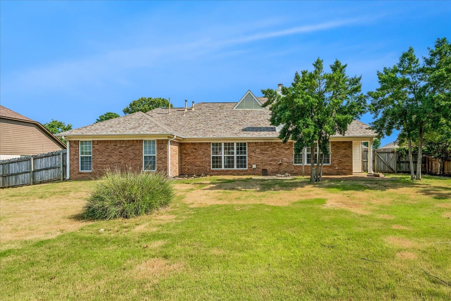6335 Needle Ridge Road Bartlett, TN 38135 - Photo 25 of 25 Rear exterior featuring brick siding, a gabled roofline, multiple windows, an outdoor patio, and mature trees