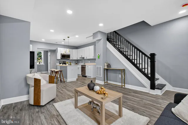a living room with couches kitchen view and kitchen view with wooden floor