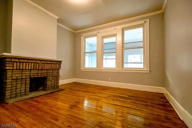 a view of an empty room with wooden floor fireplace and a window