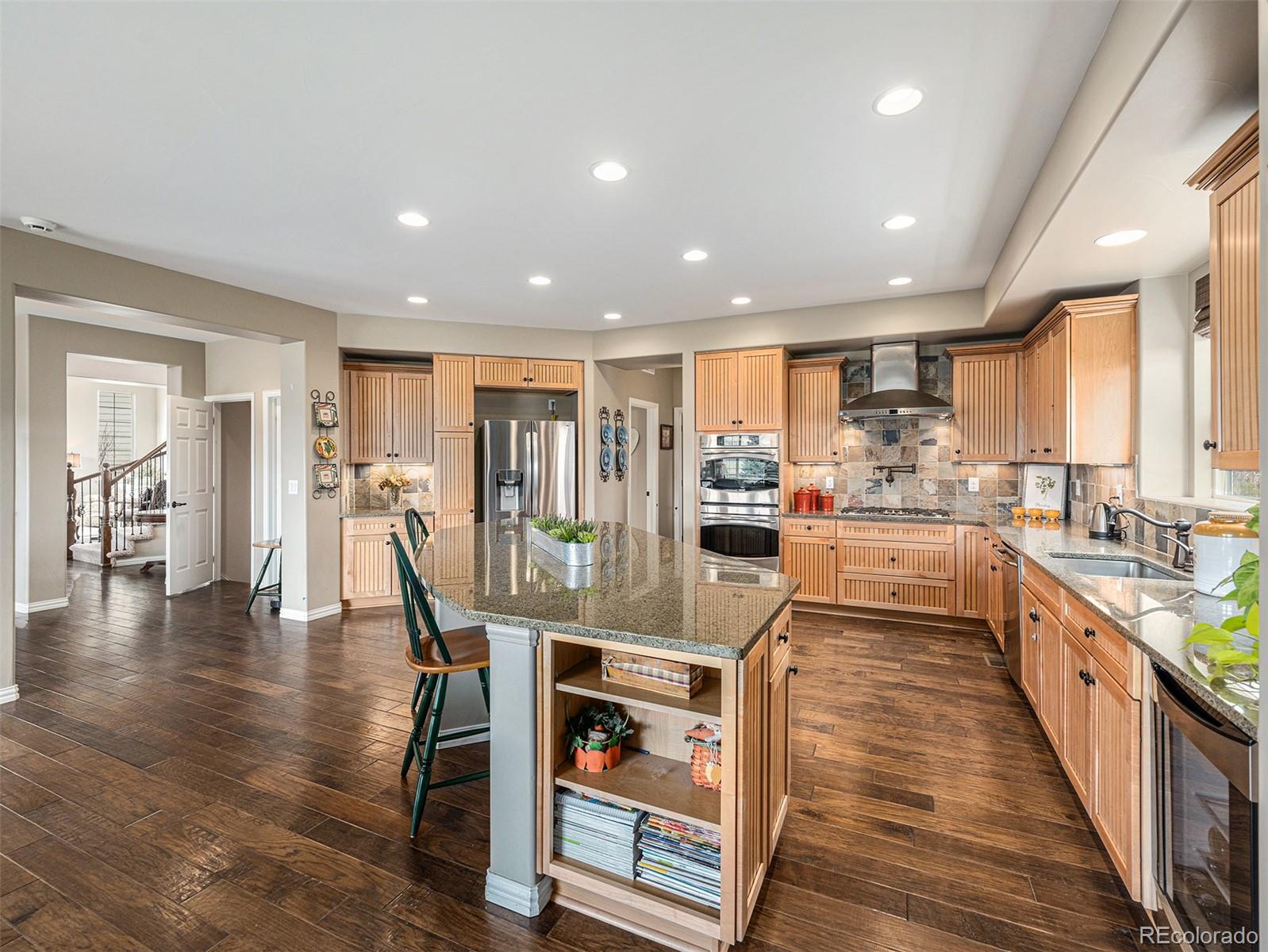 a kitchen with stainless steel appliances granite countertop wooden floor a center island and a refrigerator
