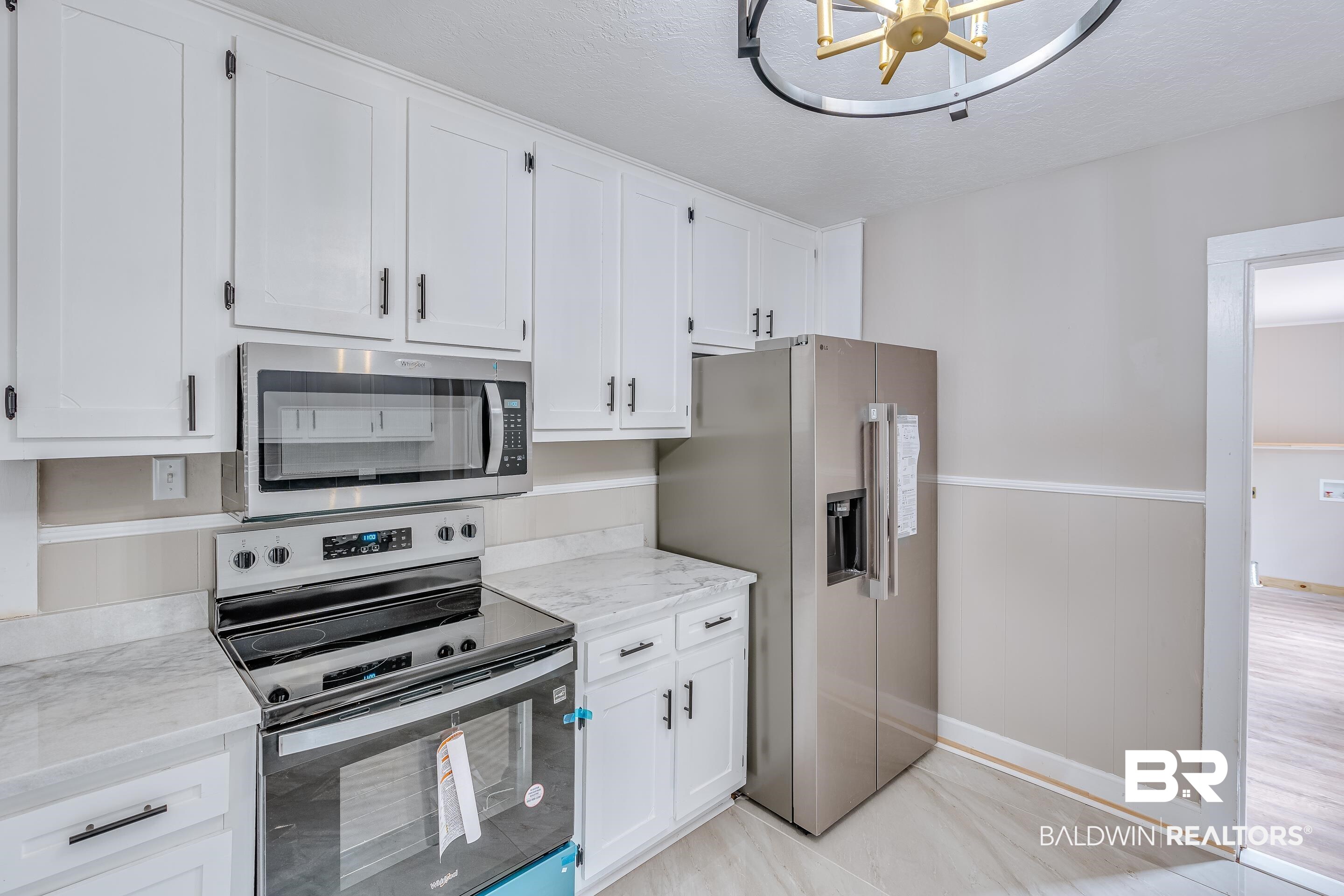 8001 16th Street Irvington, AL 36544 - Photo 15 of 35 Kitchen featuring stainless steel appliances, wainscoting, white cabinets, light stone counters, and a textured ceiling