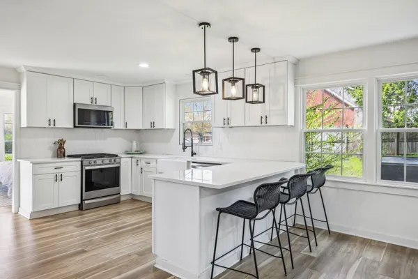 a kitchen with stainless steel appliances granite countertop a stove a sink a microwave a refrigerator and white cabinets with wooden floor