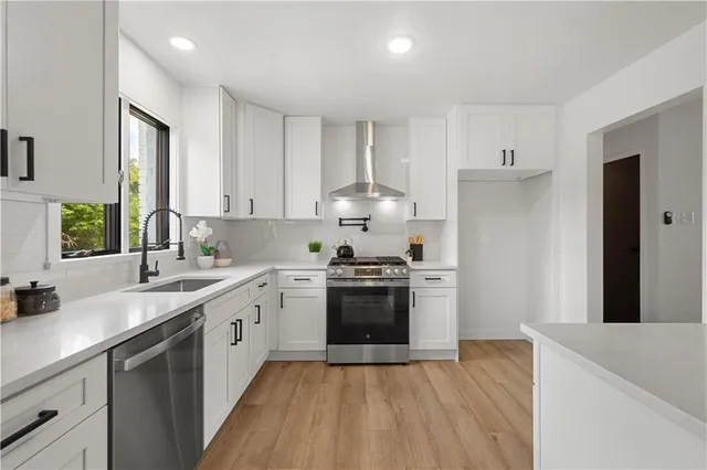 a kitchen with stainless steel appliances a stove top oven a sink dishwasher and a refrigerator with wooden floor