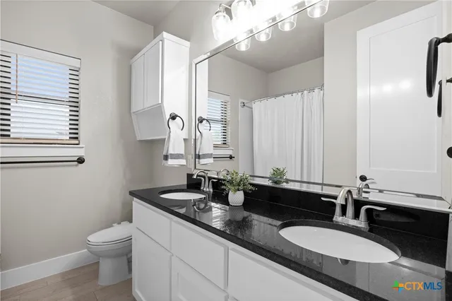 a bathroom with a granite countertop double vanity sinks a mirror a lamp and a window