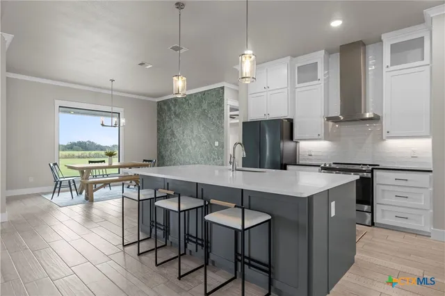 a kitchen with stainless steel appliances granite countertop a stove a refrigerator a kitchen island a dining table and chairs with wooden floor