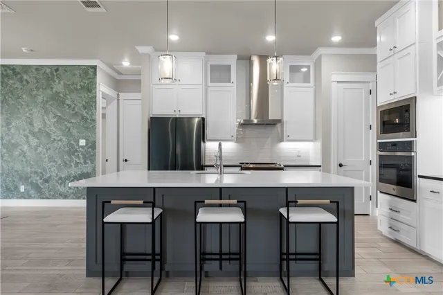 a kitchen with stainless steel appliances a sink a stove a refrigerator with white cabinets and wooden floor