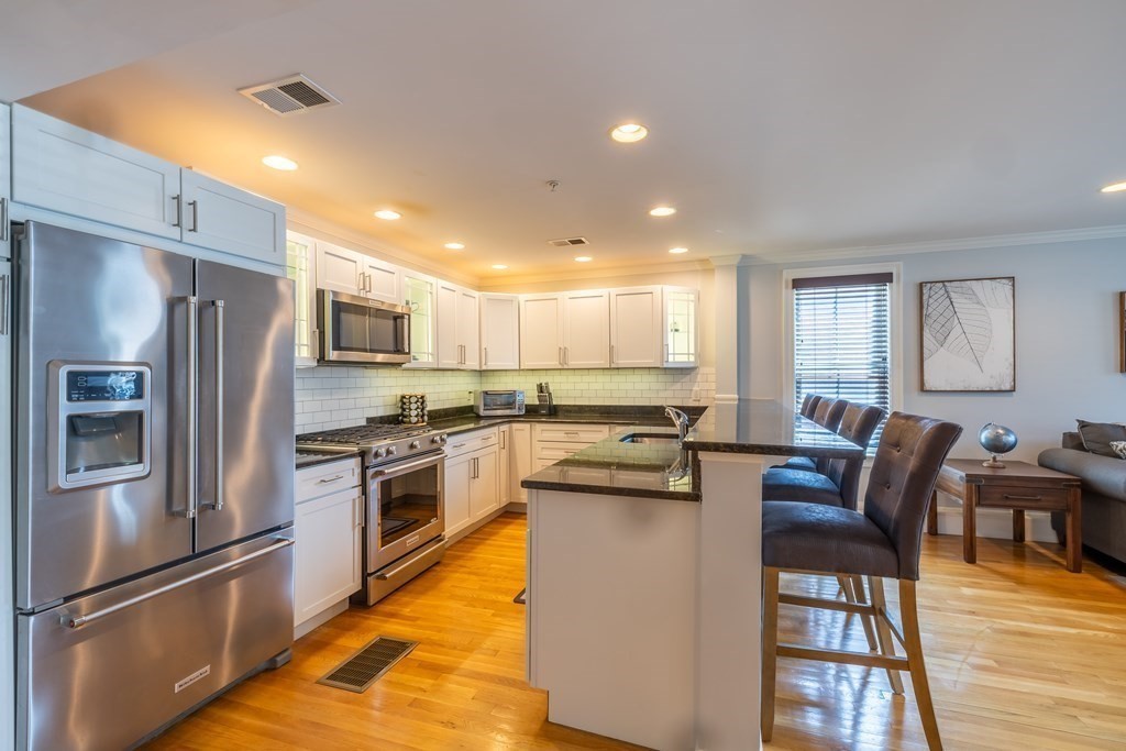 75 Main Street, Unit 102 Amesbury, MA 01913 - Photo 3 of 28 a kitchen with stainless steel appliances granite countertop a refrigerator a stove a sink a dining table and chairs with wooden floor