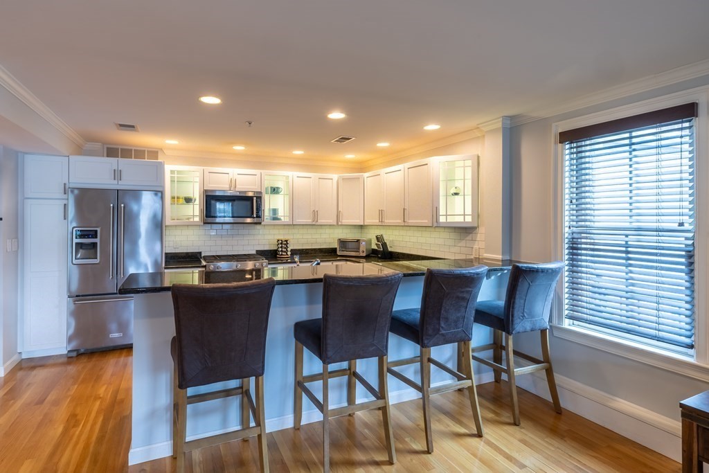 75 Main Street, Unit 102 Amesbury, MA 01913 - Photo 8 of 28 a kitchen with stainless steel appliances granite countertop a dining table chairs refrigerator and sink