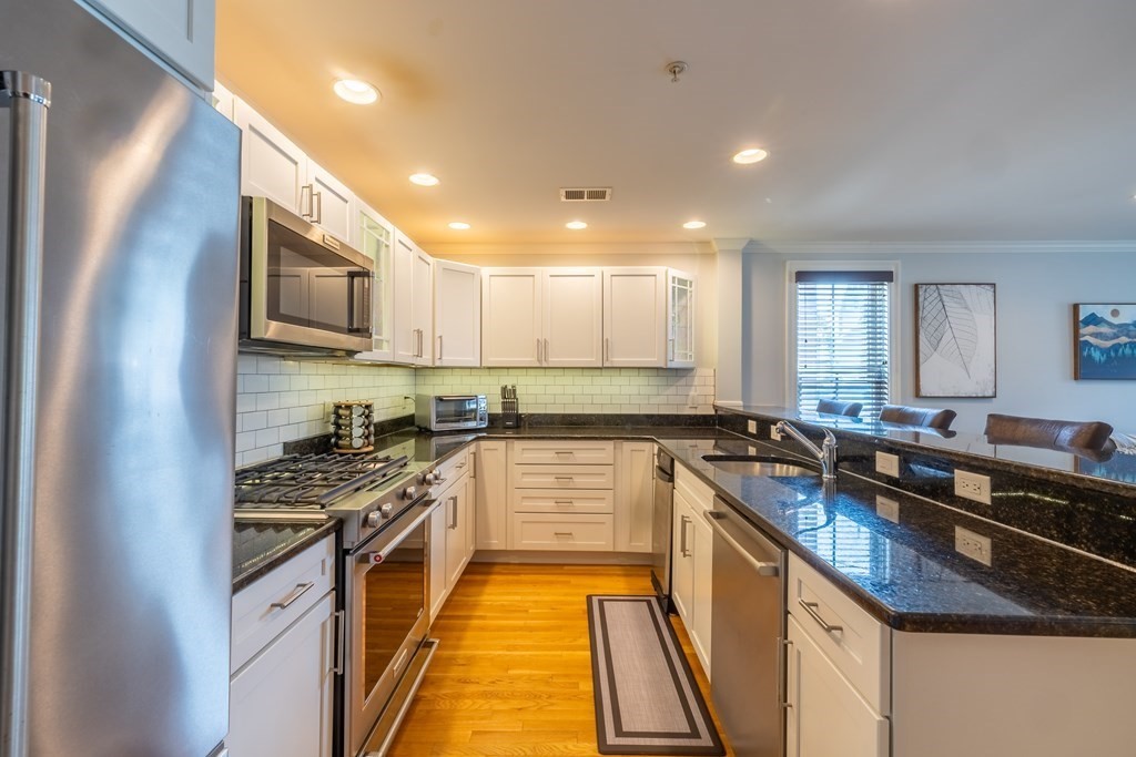 75 Main Street, Unit 102 Amesbury, MA 01913 - Photo 9 of 28 a kitchen with kitchen island granite countertop a sink a counter top space stainless steel appliances and cabinets