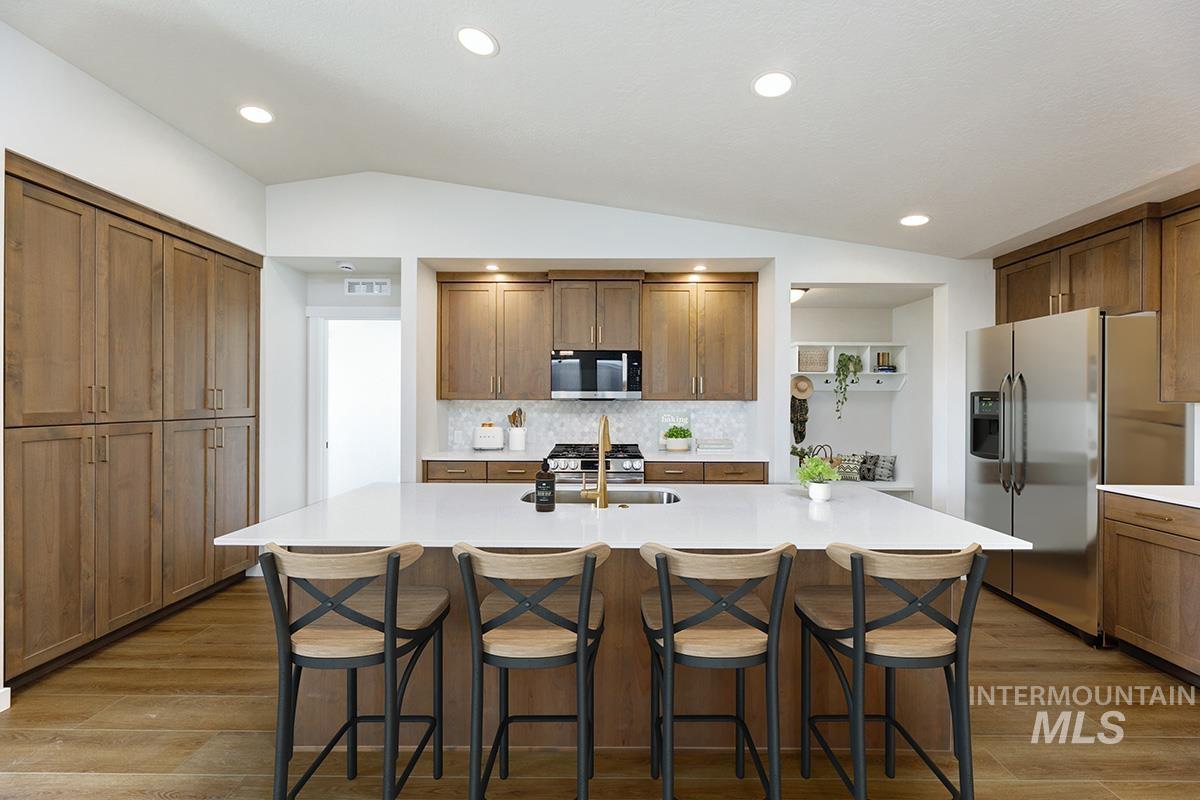 1700 East Hadler Street Meridian, ID 83642 - Photo 4 of 25 Kitchen featuring vaulted ceiling, wood finish cabinetry, tasteful backsplash, a kitchen bar, and a center island with sink