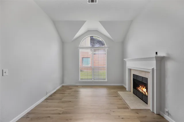 an empty room with wooden floor fireplace and windows