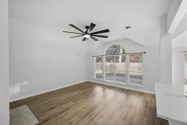 an empty room with wooden floor fan and windows