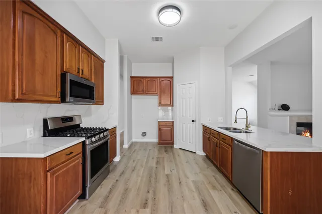 a kitchen with stainless steel appliances a stove top oven a sink dishwasher and wooden cabinets with wooden floor