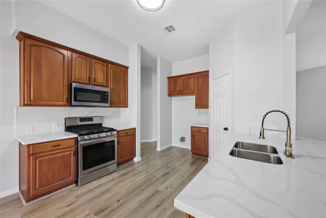 a kitchen with stainless steel appliances granite countertop a stove top oven a sink dishwasher and a microwave with wooden floor