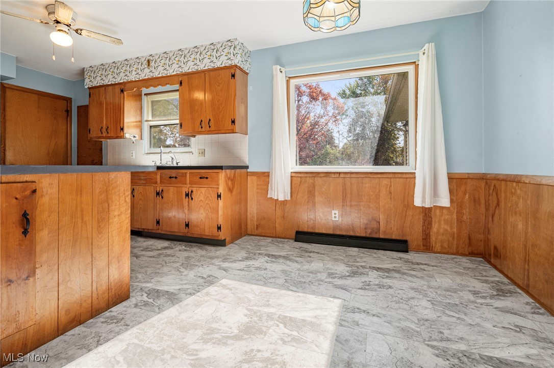 3966 Wadsworth Road Barberton, OH 44203 - Photo 9 of 28 Kitchen with brown cabinets, a wainscoted wall, wood walls, backsplash, and a baseboard heating unit