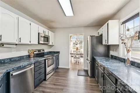 a kitchen with stainless steel appliances granite countertop a stove top oven a sink dishwasher a refrigerator and a granite counter tops with wooden floors