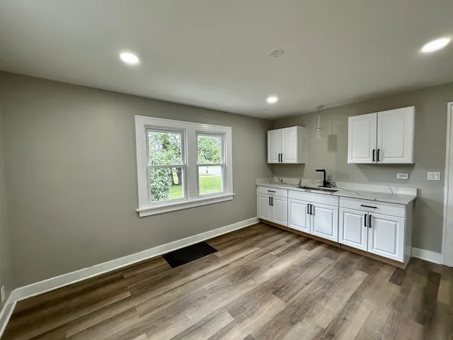 a large kitchen with stainless steel appliances granite countertop a stove a sink white cabinets and a wooden floor