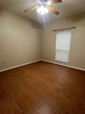 an empty room with wooden floor fan and windows