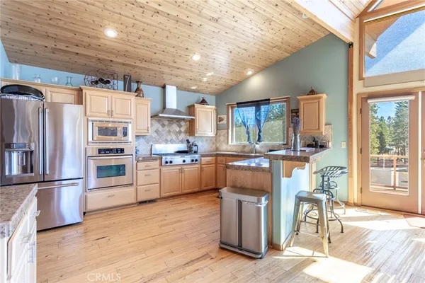 a kitchen with stainless steel appliances kitchen island granite countertop a refrigerator a stove a sink dishwasher and a dining table with wooden floor