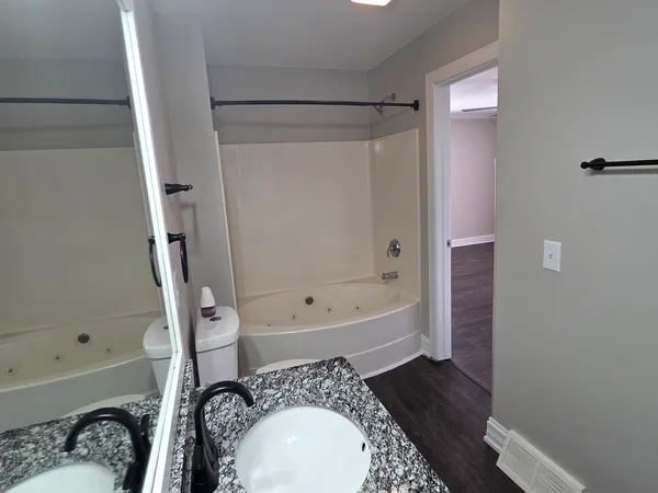 a bathroom with a granite countertop bathtub sink vanity mirror and toilet