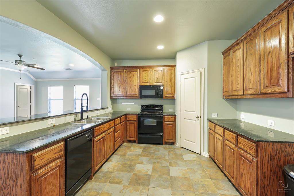 6601 Pine Hills Lane Denton, TX 76210 - Photo 5 of 23 Kitchen with black appliances, brown cabinetry, a ceiling fan, dark stone counters, and arched walkways