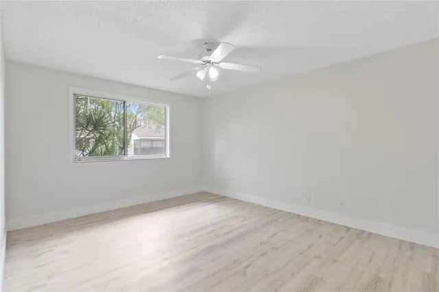 an empty room with wooden floor chandelier fan and windows