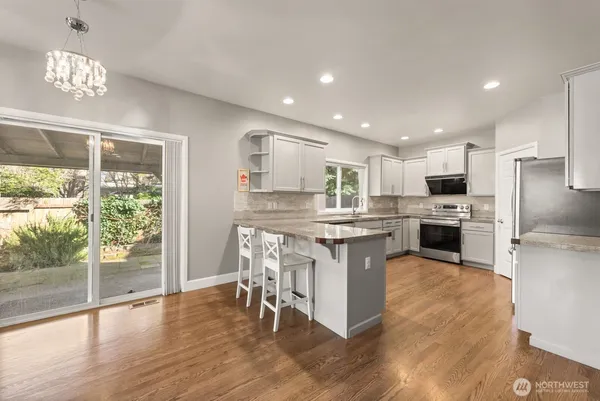 a kitchen with granite countertop a stove a sink a refrigerator and a dining table with wooden floor
