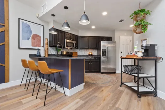 a kitchen with stainless steel appliances kitchen island granite countertop a stove a refrigerator a sink a dining table and chairs with wooden floor