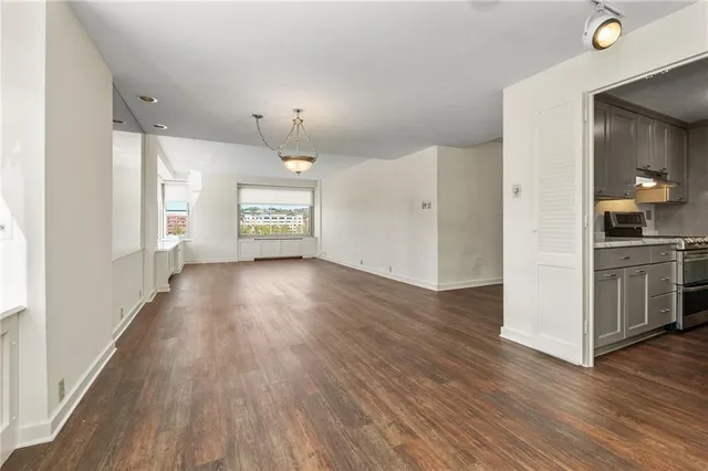 a view of a hallway to an empty room with wooden floor and a window