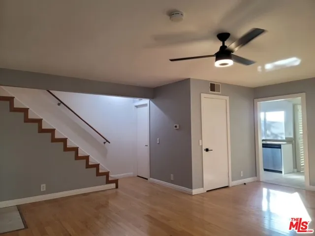 a view of an empty room with wooden floor and a ceiling fan