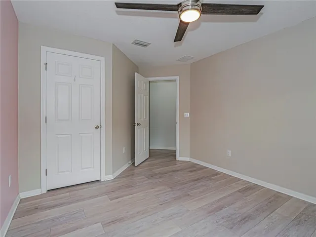 an empty room with wooden floor chandelier fan and windows